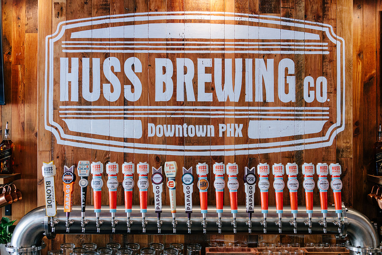 Huss Brewing Co. logo on a wall over various beer taps