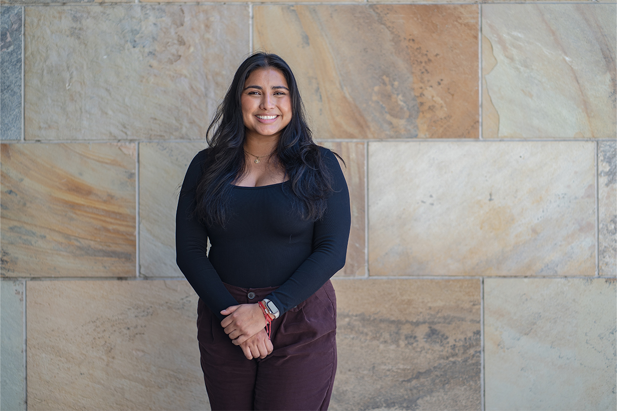 A smiling woman standing in front of an exterior wall 