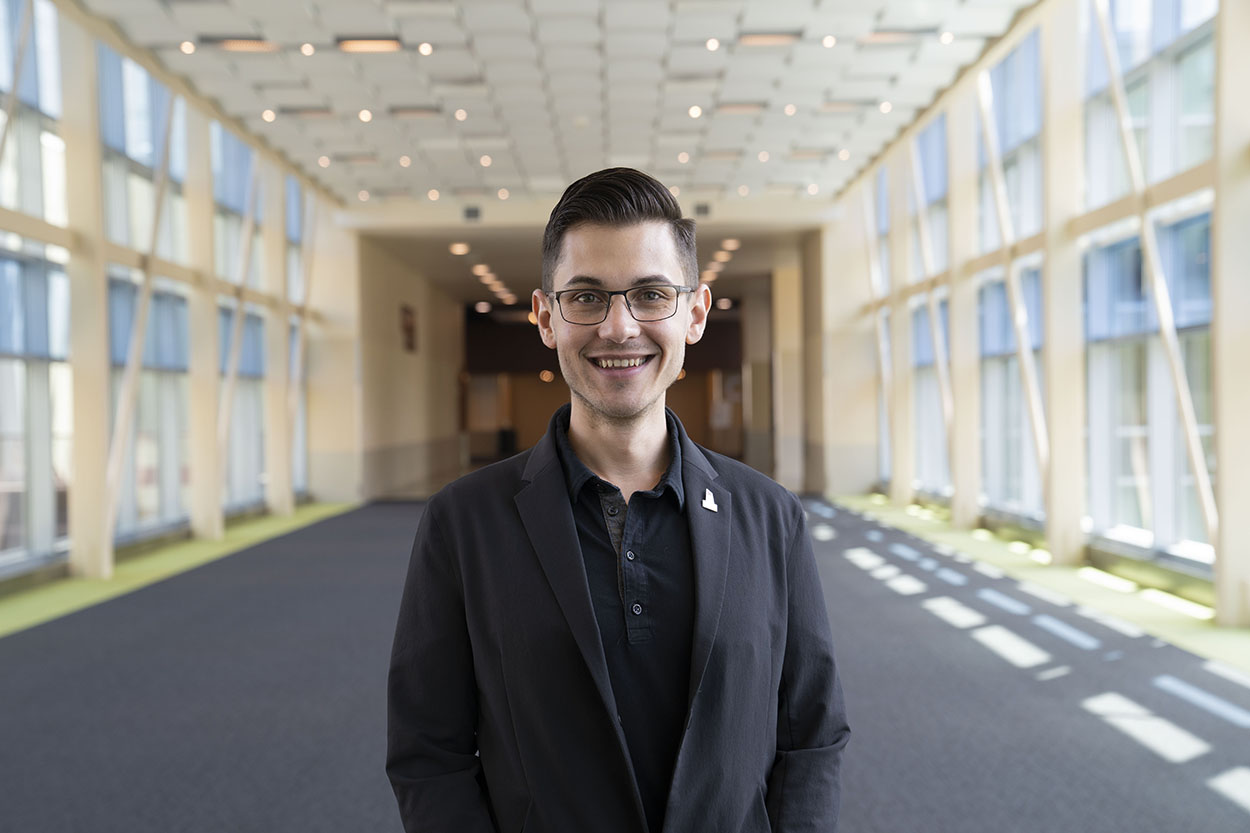 Headshot of a man standing in a long hallway with windows