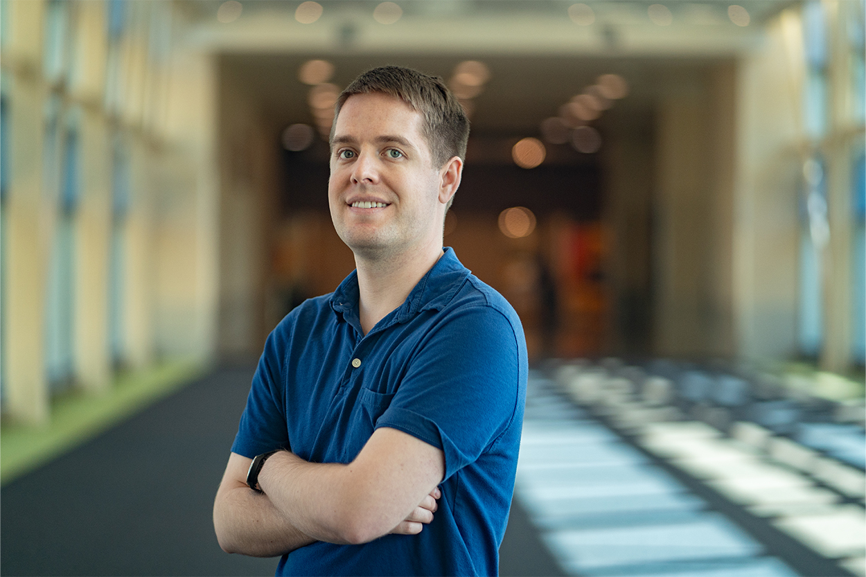 Headshot of a man standing in a long hallway with windows