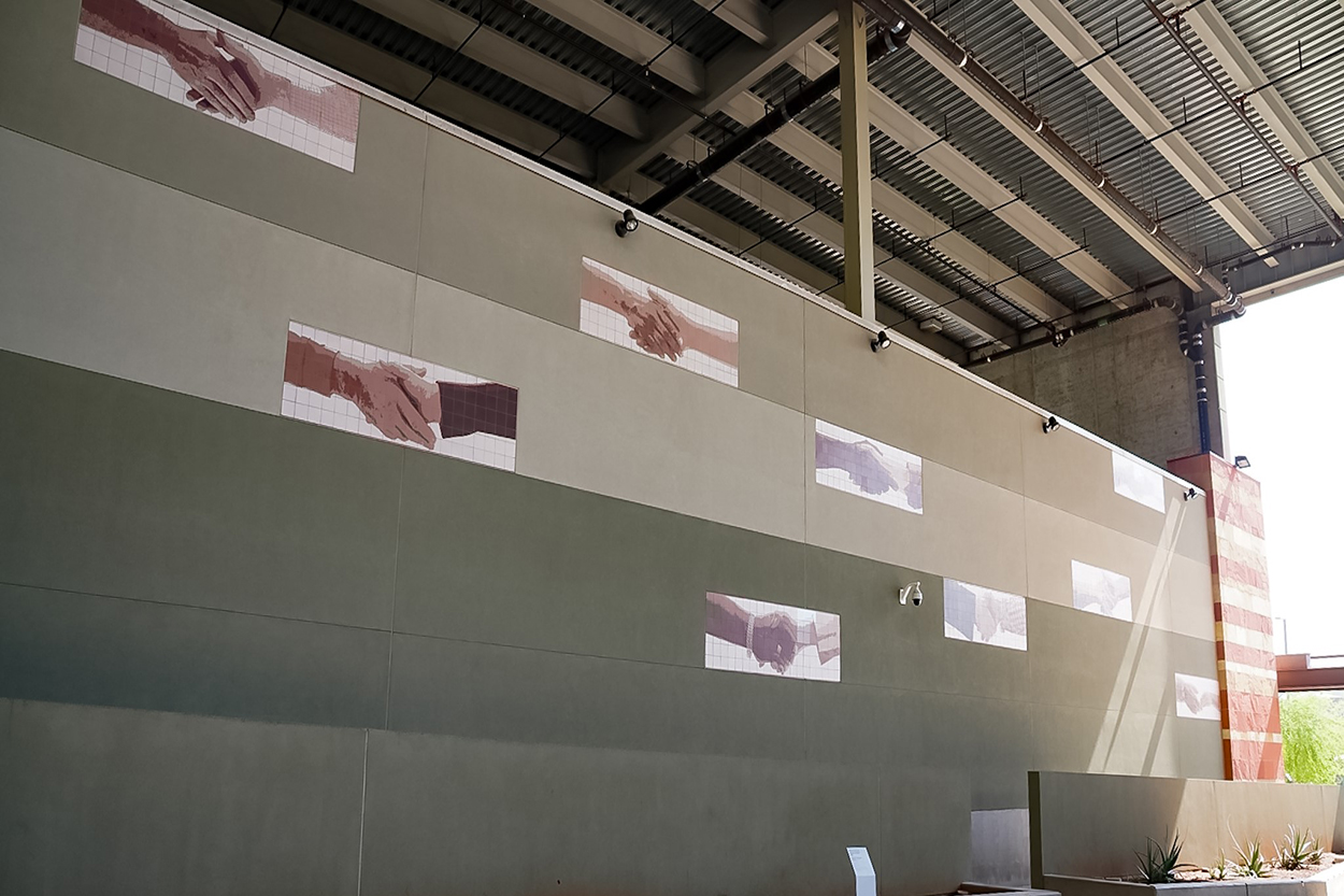 Tilography artwork depicting handsakes is mounted on an exterior wall