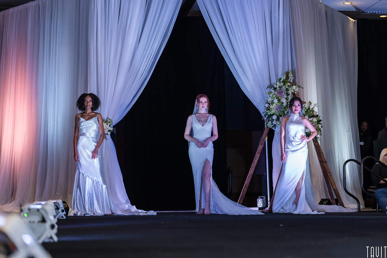 Three female models wearing wedding gowns on a stage
